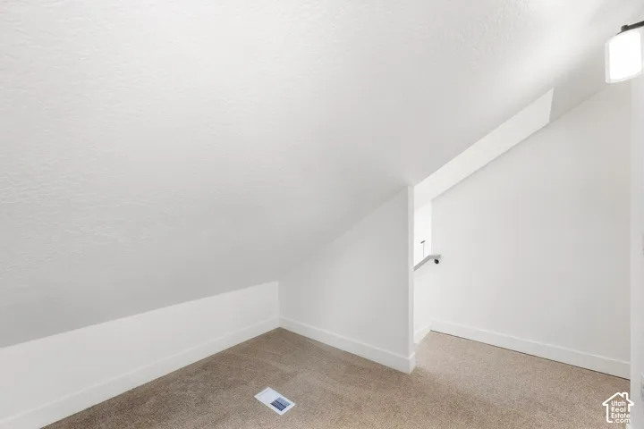 Sloped ceiling room featuring neutral carpeting, white walls, and a wall-mounted light fixture