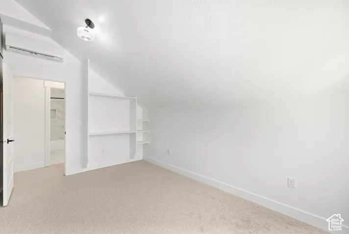 Vaulted ceiling room with built-in shelving, carpet flooring, and an attached light fixture