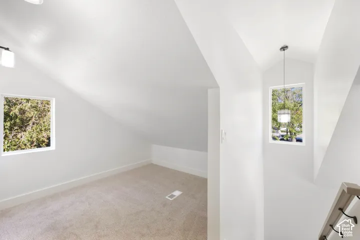 Angled ceilings, neutral carpet, recessed lighting, white trim, and a contemporary pendant light