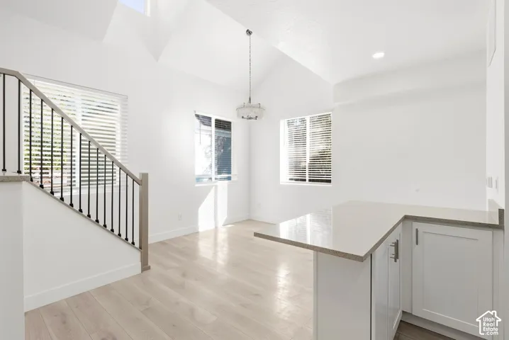 Vaulted ceilings with a skylight, light wood-finish flooring, a kitchen peninsula with light countertops, white cabinetry, and a staircase with a black metal railing