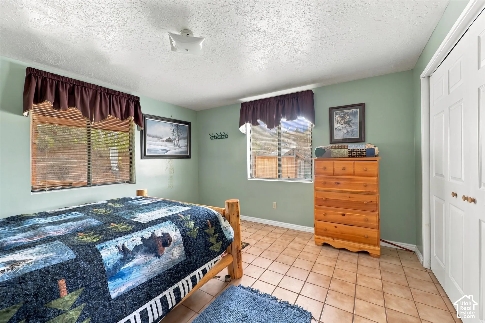 Tile flooring, two windows with blinds, light green wall color, a flush-mount ceiling light fixture, and a white bi-fold closet door