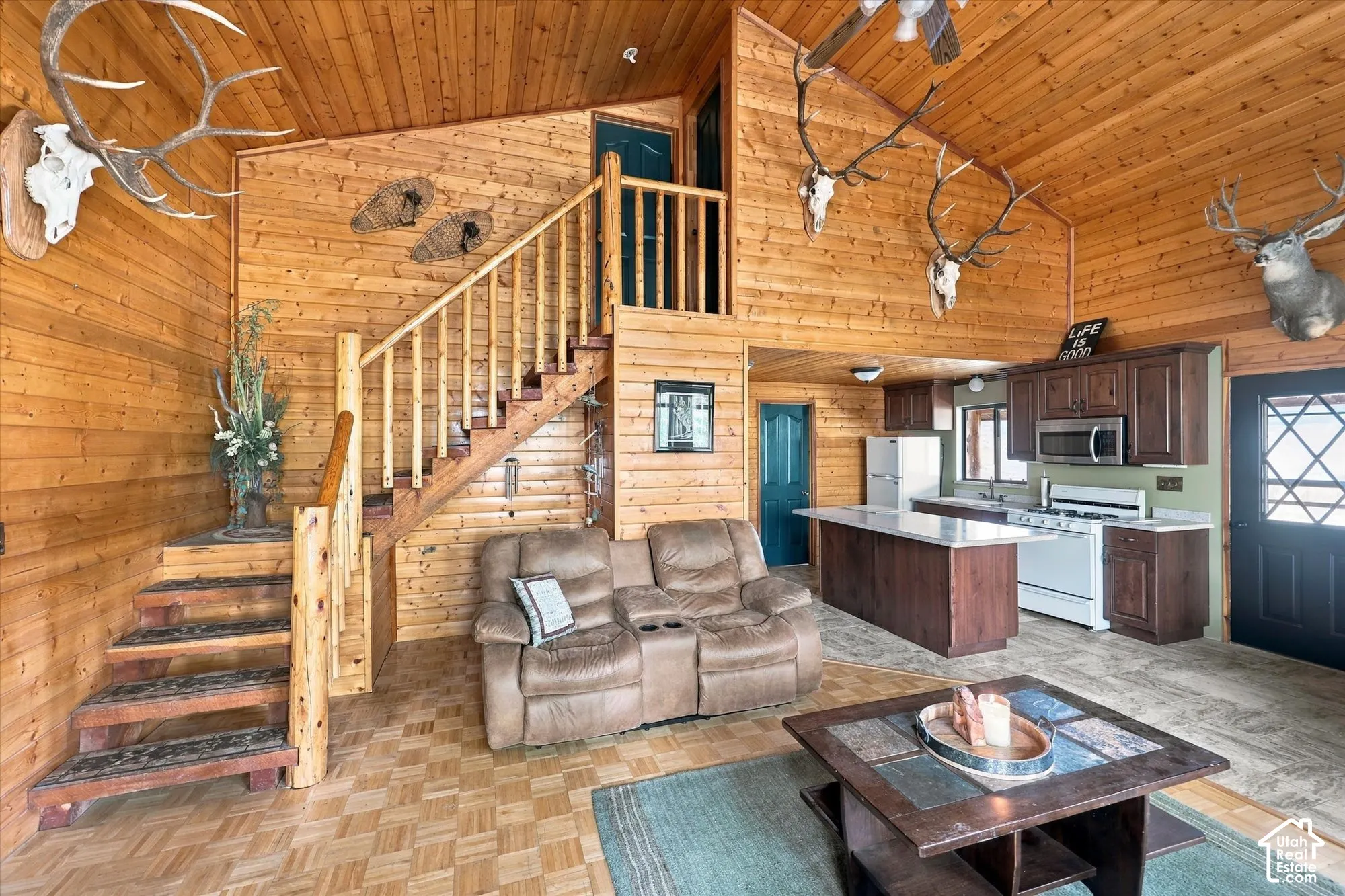 Vaulted wood-paneled ceilings, wood-finish flooring, wood staircase with log newel post, kitchen island with solid surface countertop, and wood cabinetry