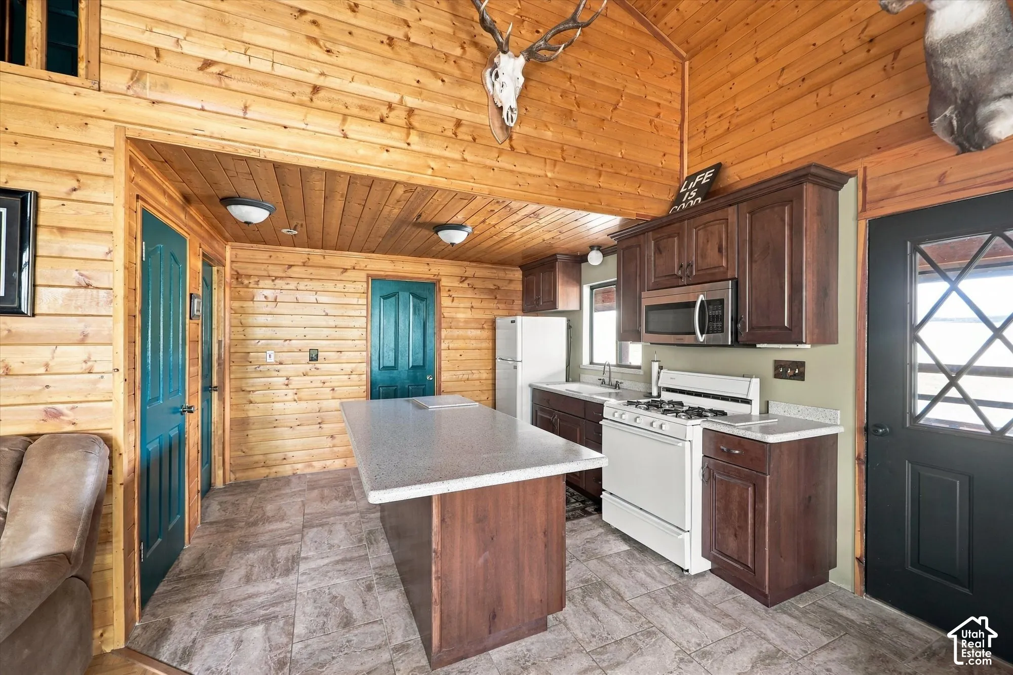 Wood-paneled interior featuring vaulted ceilings, a kitchen island with a light-toned countertop, dark wood-finish cabinetry, and a black exterior door with window panes
