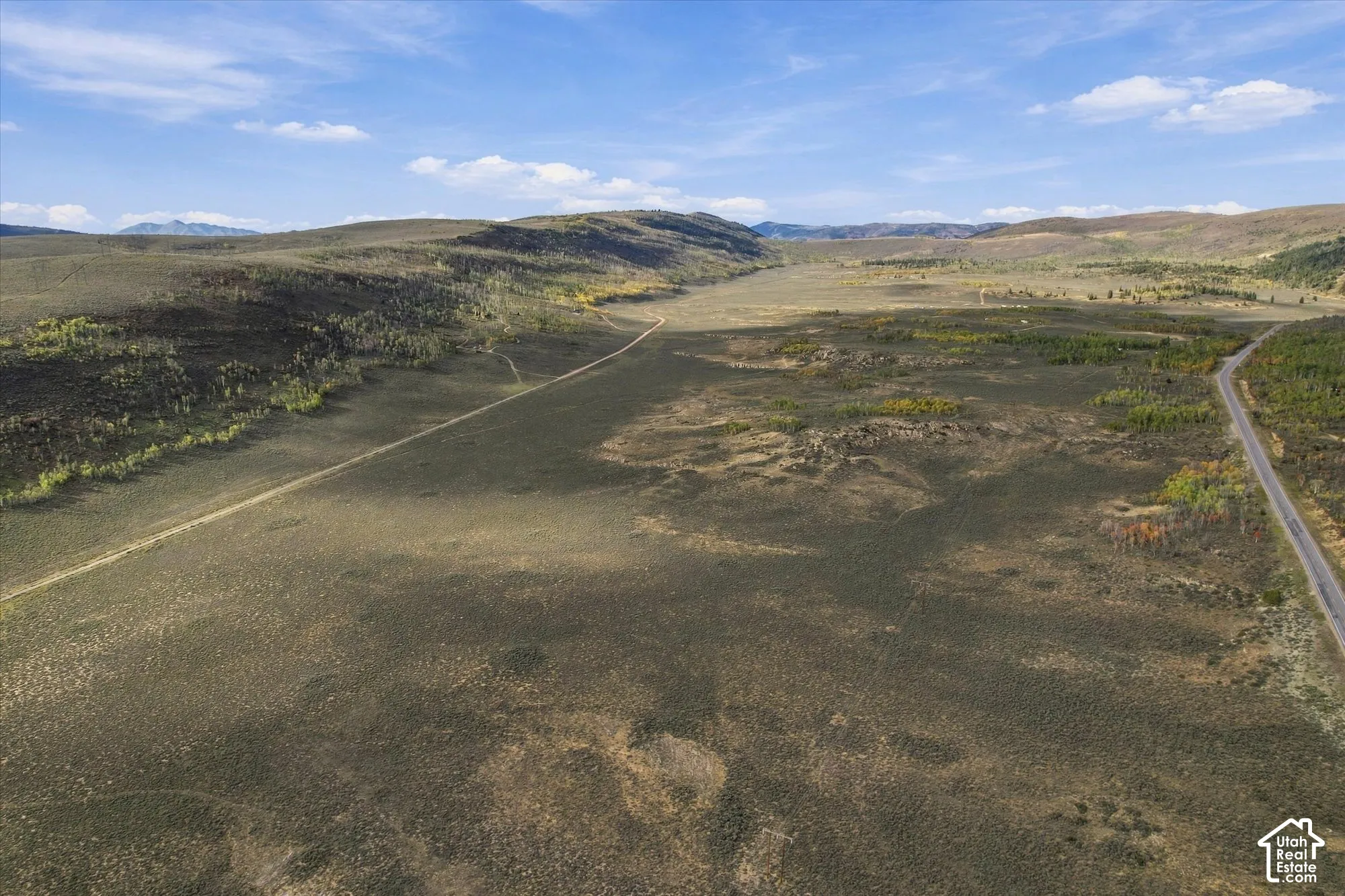 Expansive natural landscape with rolling hills, a paved road, and a dirt road