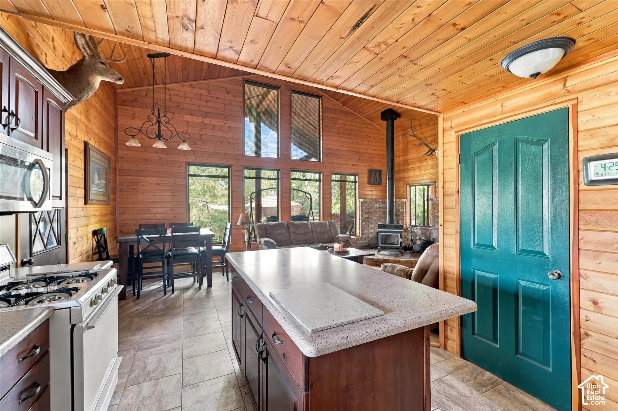 Open-concept living space featuring wood-paneled walls and ceiling, a kitchen island with a light-toned countertop, a stainless steel gas range, and large windows