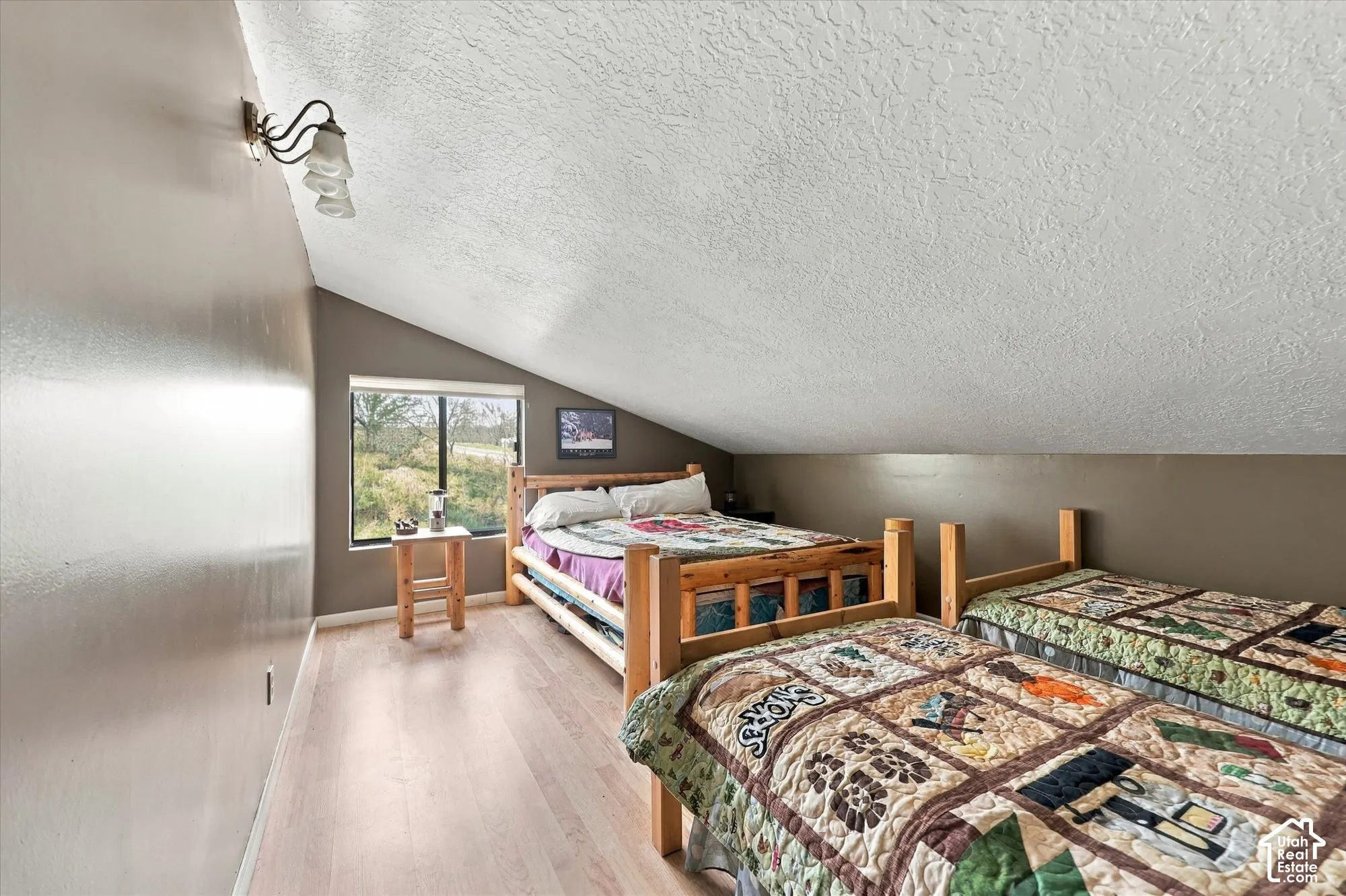 Angled ceiling with a textured finish, light wood-finish flooring, and a fixed window overlooking greenery
