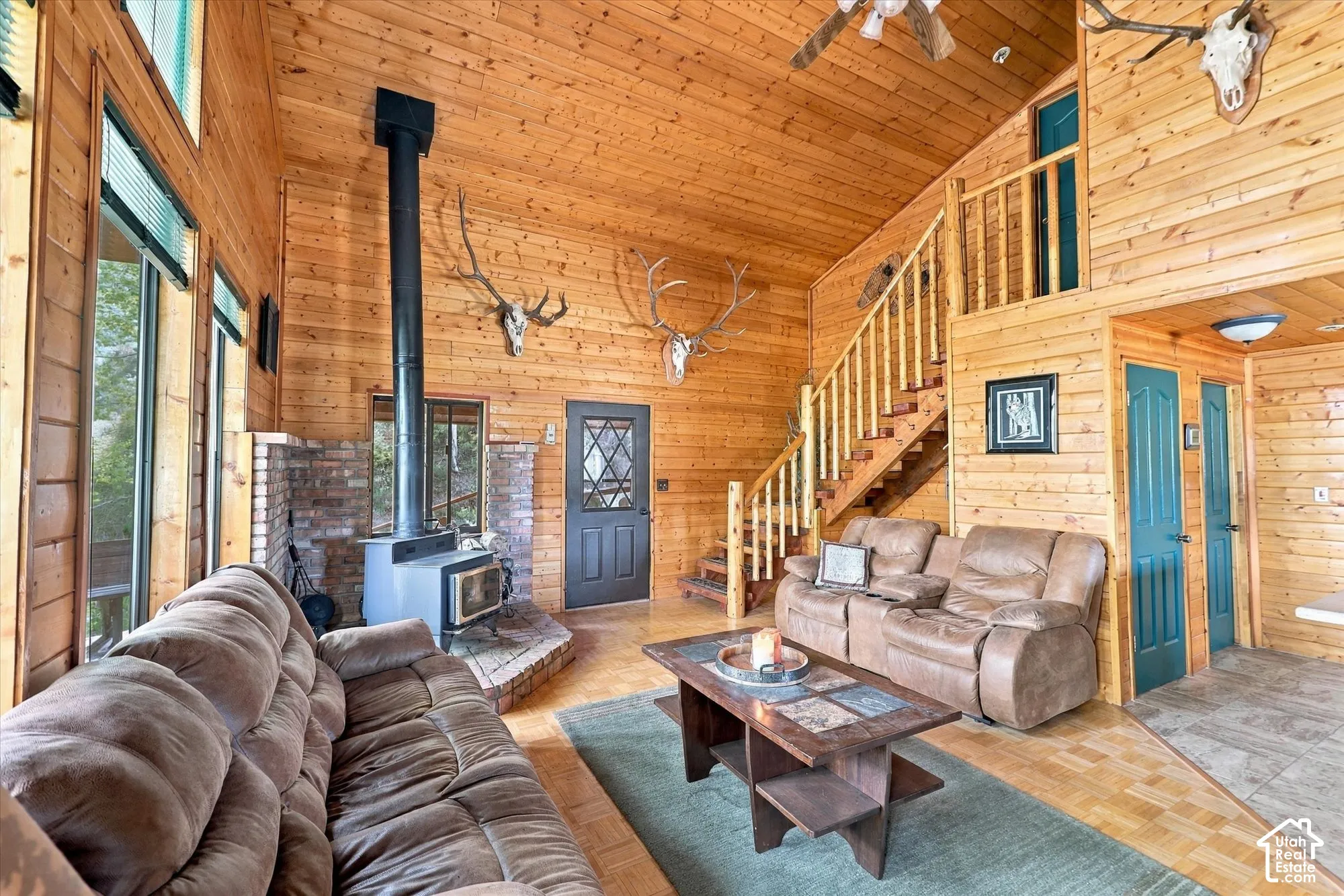 Vaulted wood-paneled ceilings, wood-finish flooring, a wood-burning stove with brick surround, and a wooden staircase with railing