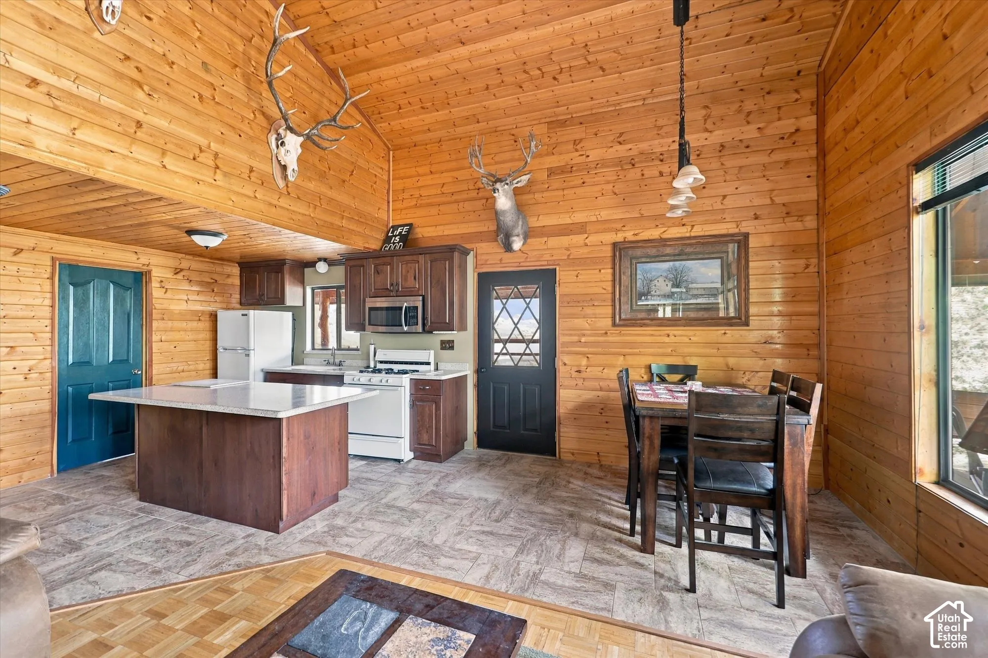 Wood-paneled vaulted ceilings and walls, kitchen island with solid surface countertop, wood-finish cabinetry, built-in microwave, and tile-look flooring