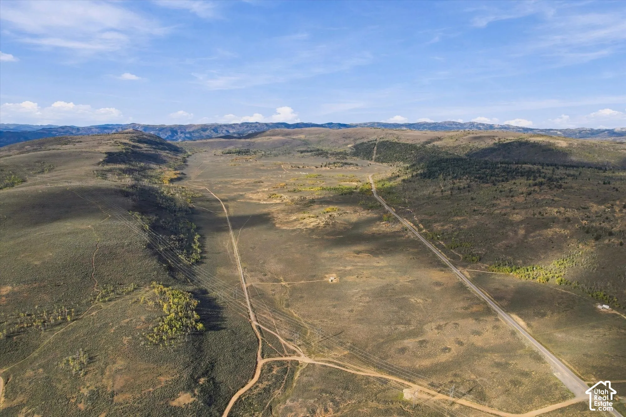 Expansive rural landscape featuring a paved road, dirt paths, scattered trees, and distant mountains