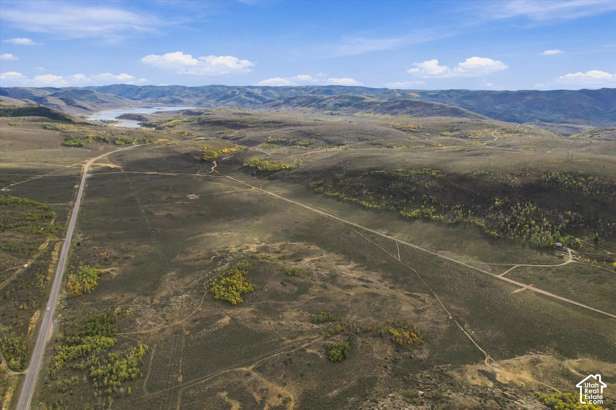 Expansive undeveloped acreage with a lake, mountains, natural vegetation, and a paved road