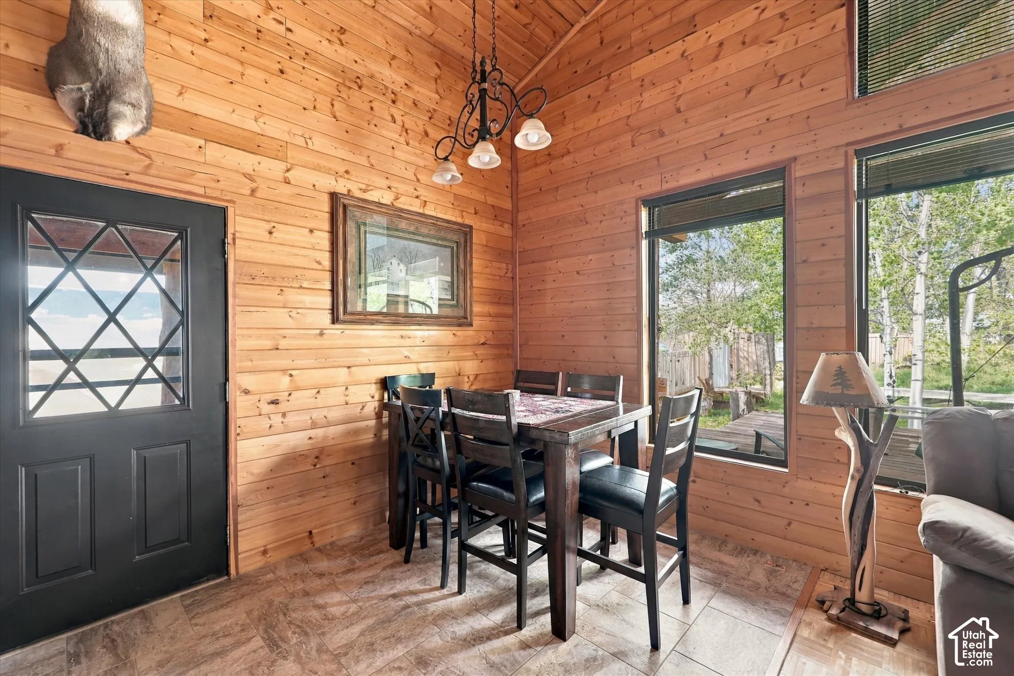 Wood-paneled interior walls with a vaulted ceiling, large windows, and a black exterior door with decorative lites