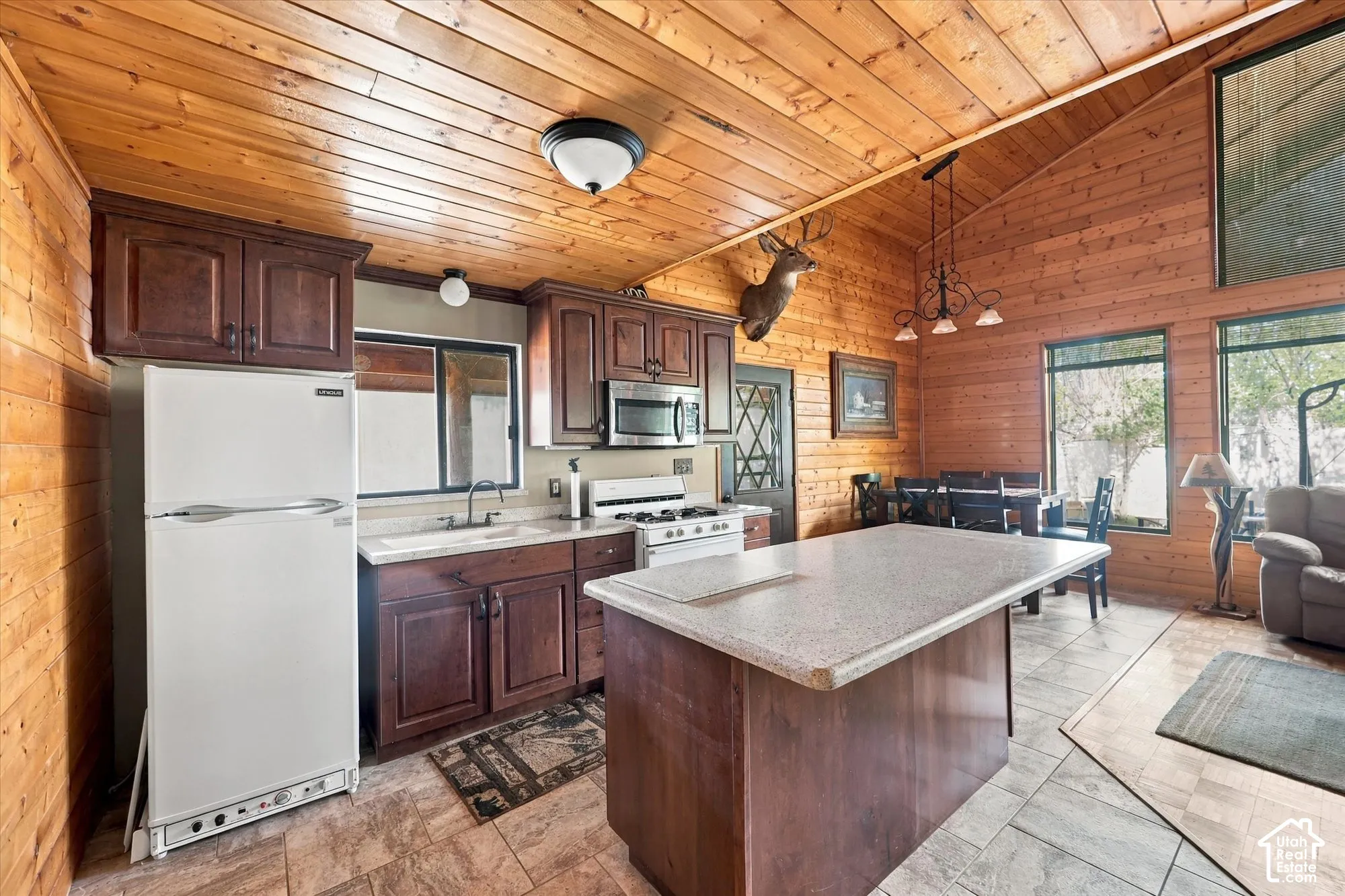 Wood-paneled walls and ceilings, vaulted ceiling, kitchen island with solid surface countertop, dark wood-finish cabinetry, and tiled flooring
