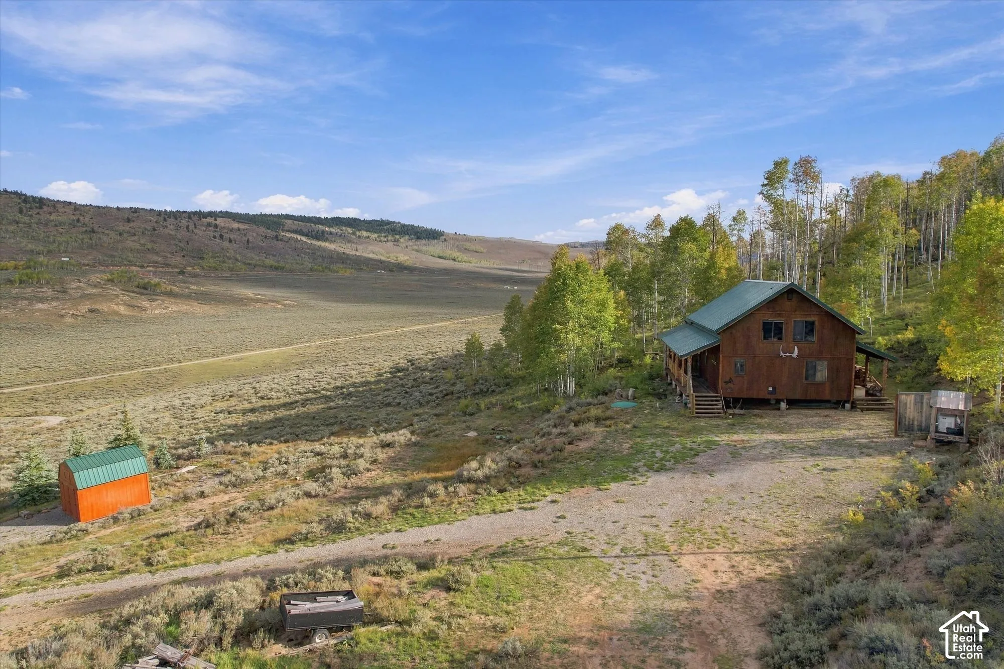Wood-sided dwelling with a green pitched roof, surrounded by mature trees and natural terrain