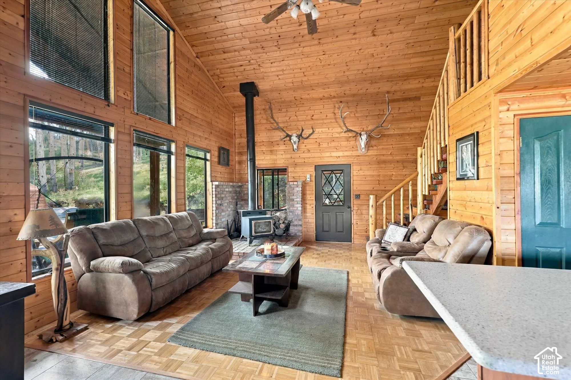 Wood-paneled walls and ceiling, a wood-burning stove with a brick surround, and a ceiling fan with light fixture