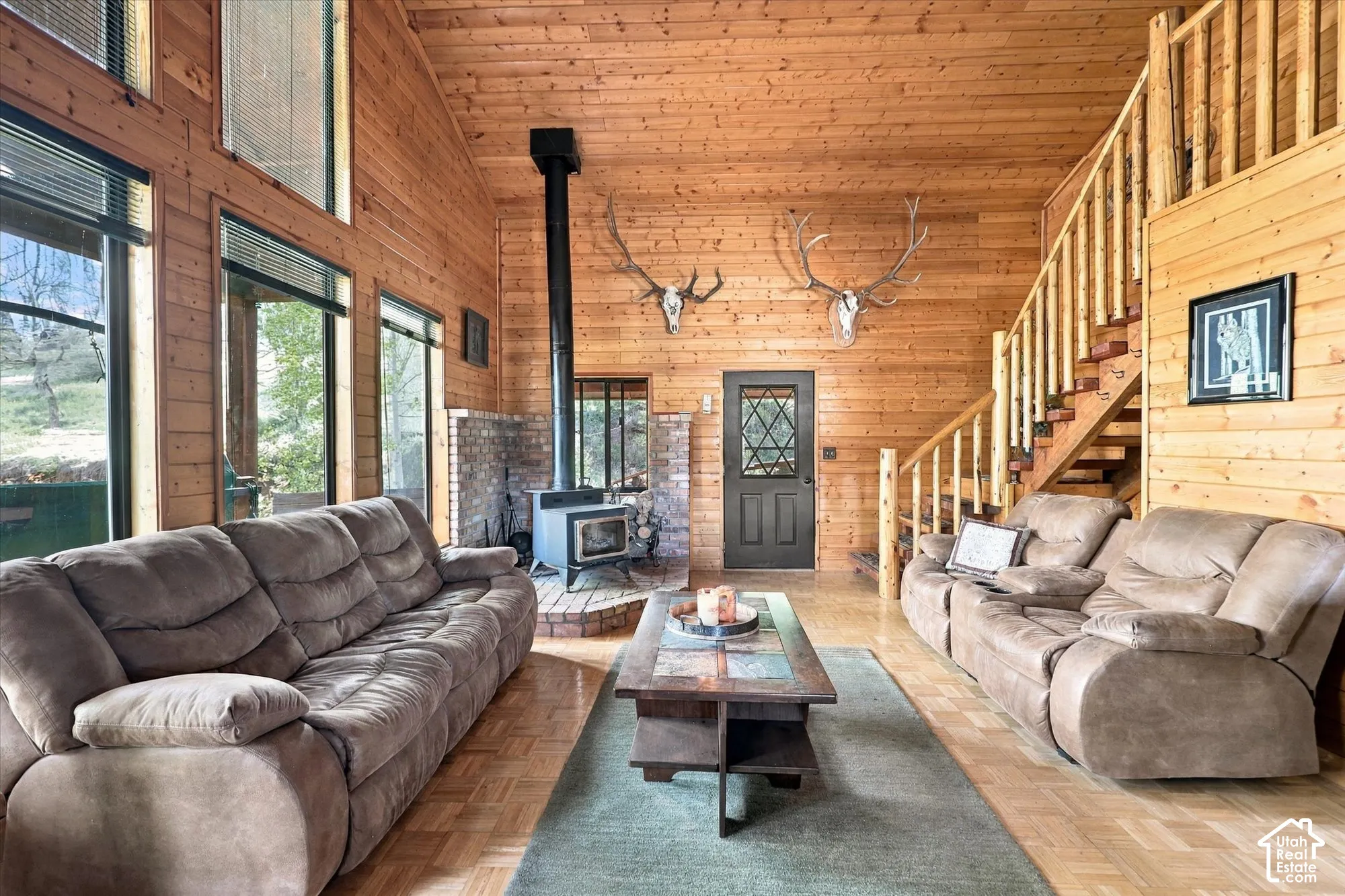 Vaulted wood-paneled ceiling, wood-finish flooring, wood-burning stove with brick surround, multi-pane entry door, and a prominent wood staircase