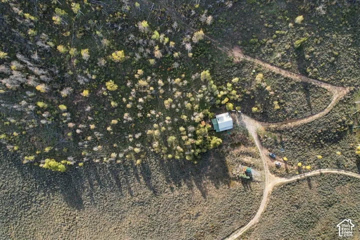 Expansive natural landscape featuring a single-story structure with a gabled roof, surrounded by varied vegetation and multiple unpaved paths