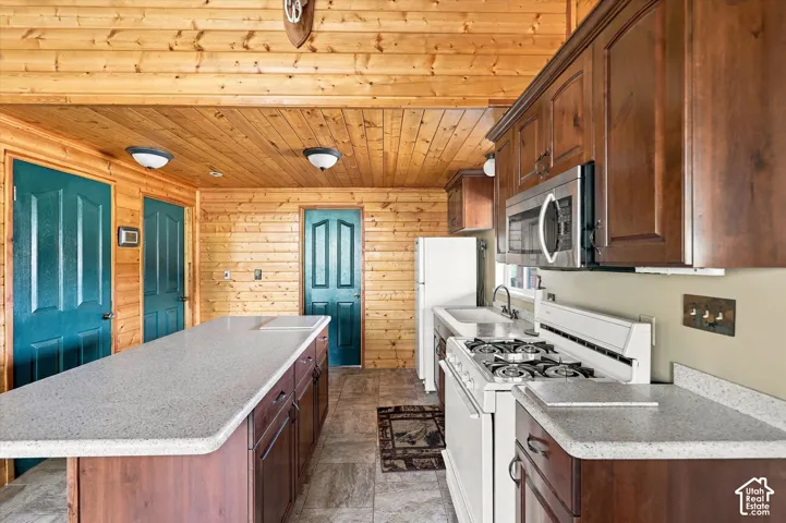 Spacious kitchen featuring wood cabinetry, stainless steel appliances including a gas cooktop and microwave, quartz countertops, and a large center island with seating