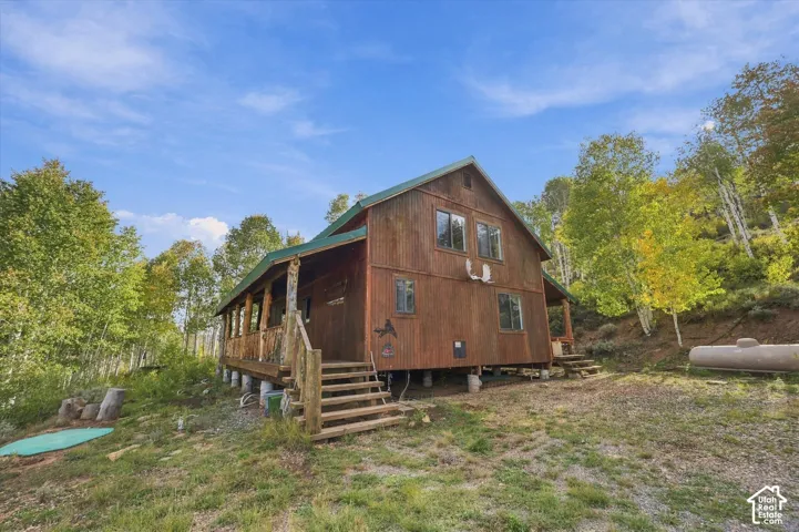 Wood-sided cabin structure featuring a covered porch with natural wood posts, multiple windows, and a sloped metal roof