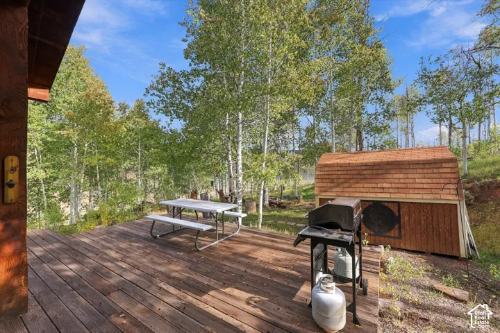 Expansive wood deck with a built-in storage shed featuring a shingled roof, surrounded by mature trees