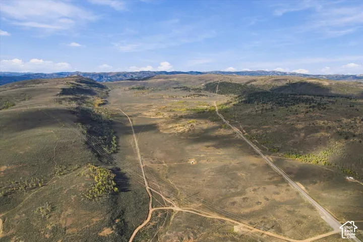 Expansive rural landscape featuring a paved road, dirt paths, scattered trees, and distant mountains