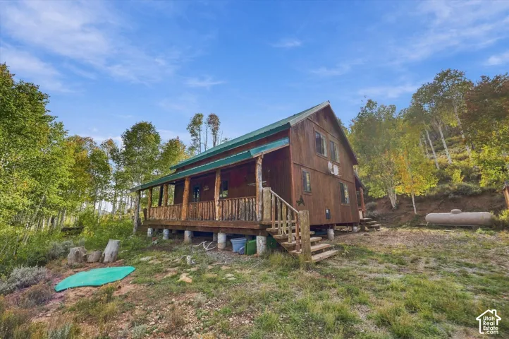 Wood-sided cabin featuring a green metal roof, a full-width covered porch with rustic log railing, and exterior stairs