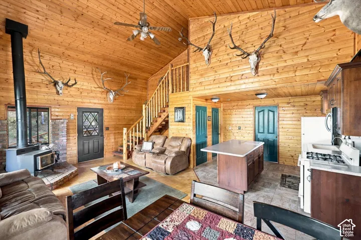 Vaulted wood-paneled ceilings with exposed beams, central wood-burning stove with brick hearth, open-concept kitchen with island, wood cabinetry, and gas range