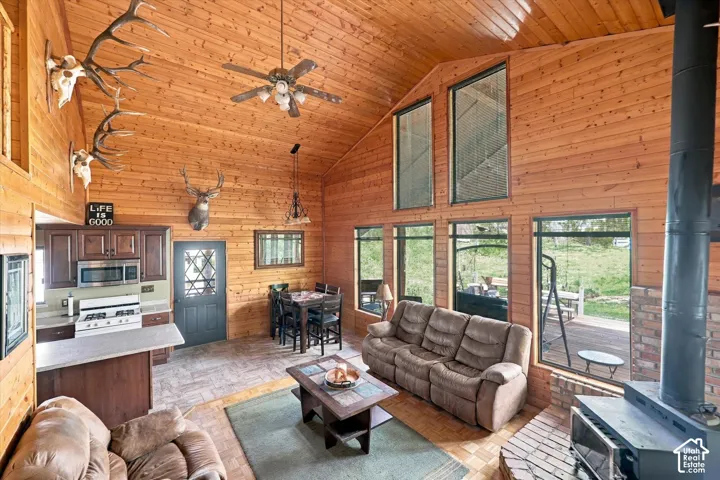 Open-concept living space showcasing vaulted wood-plank ceilings, expansive multi-pane windows framing outdoor scenery, and a wood-burning fireplace with stone surround
