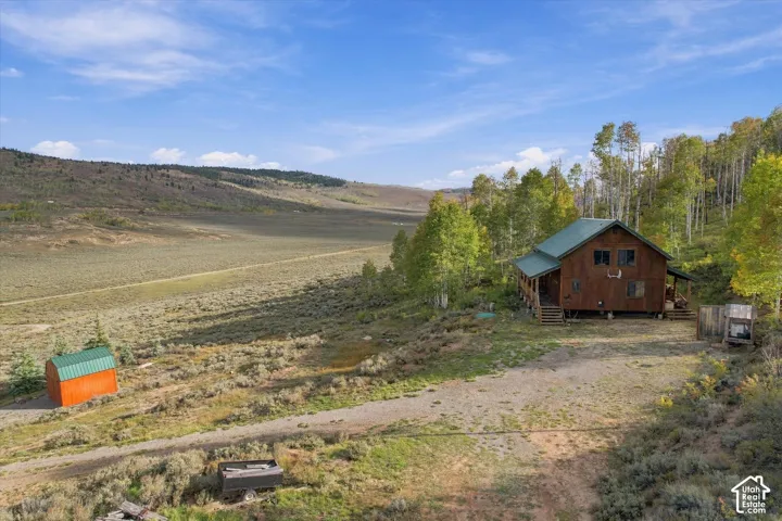 Wood-sided dwelling with a green pitched roof, surrounded by mature trees and natural terrain