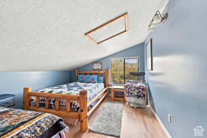Sloped ceiling with recessed skylight, wall-mounted light fixture, and wood-finish flooring