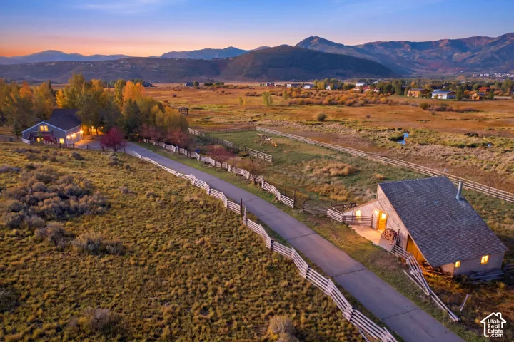 Expansive rural setting featuring a single-family residence, an additional auxiliary structure, and a split-rail fence-lined driveway