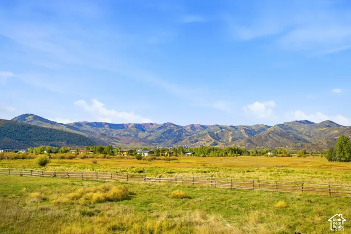 Expansive natural landscape with distant mountains, a sprawling field, and a rustic split-rail fence