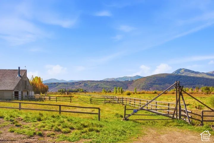 Expansive rural acreage featuring a barn with a shingle roof, natural wood fencing, and distant mountain scenery