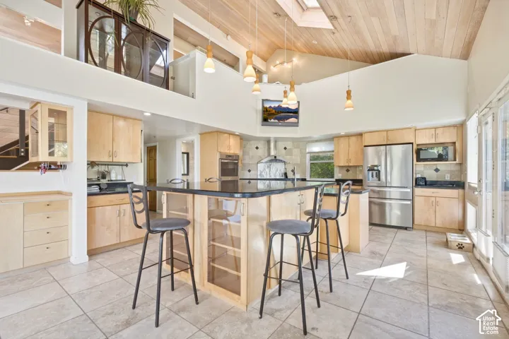 Vaulted wood-finish ceiling, skylight, recessed lighting, tile flooring, and integrated stainless steel appliances