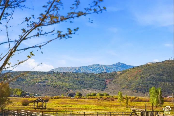 Expansive field with a rustic wooden fence and a gazebo, set against a backdrop of rolling hills and distant mountains