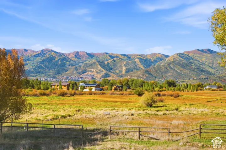 Expansive undeveloped land with a partial wood-split rail fence, surrounded by lush trees, and featuring distant mountain scenery
