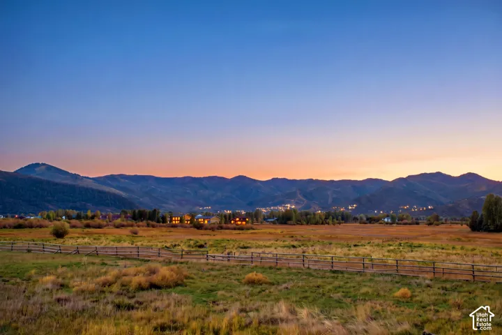 Expansive open fields with a wooden rail fence, distant mountain range, and scattered residences in the background