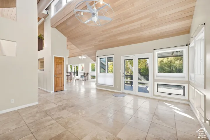 Vaulted wood-finish ceiling, tiled flooring, built-in wall paneling, and French doors leading to an exterior deck