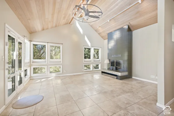 Vaulted wood-paneled ceiling, tiled flooring, built-in fireplace with hearth, multiple windows, and exterior access via double doors