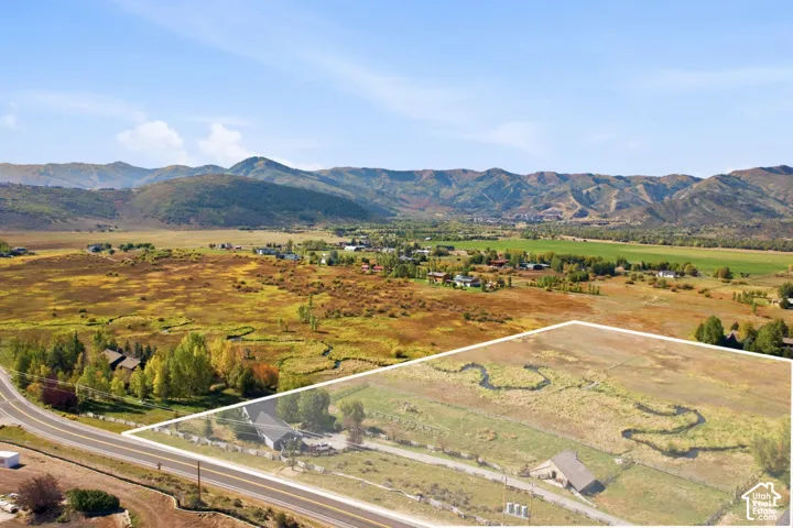 Expansive land parcel featuring a meandering stream, partial mature tree coverage, and mountain scenery
