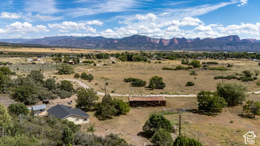 Expansive rural setting with a single-story residence, a detached shed, a secondary structure, and distant mountain ranges