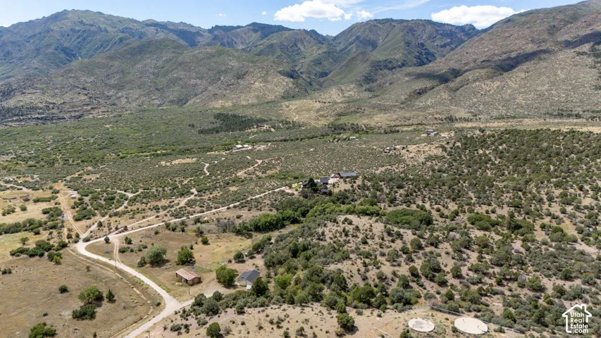 Expansive land parcel with surrounding mountains, scattered foliage, and visible structures