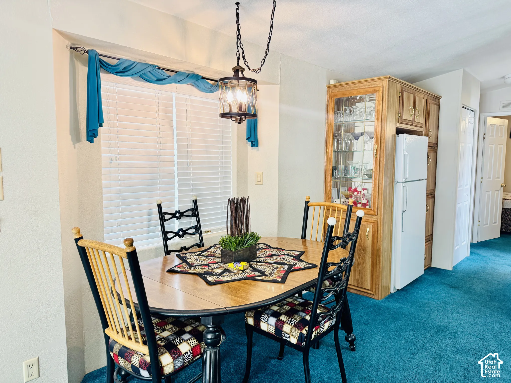 Bay window with horizontal blinds, overhead chandelier light fixture, built-in cabinetry with glass display, and light wood-finish flooring