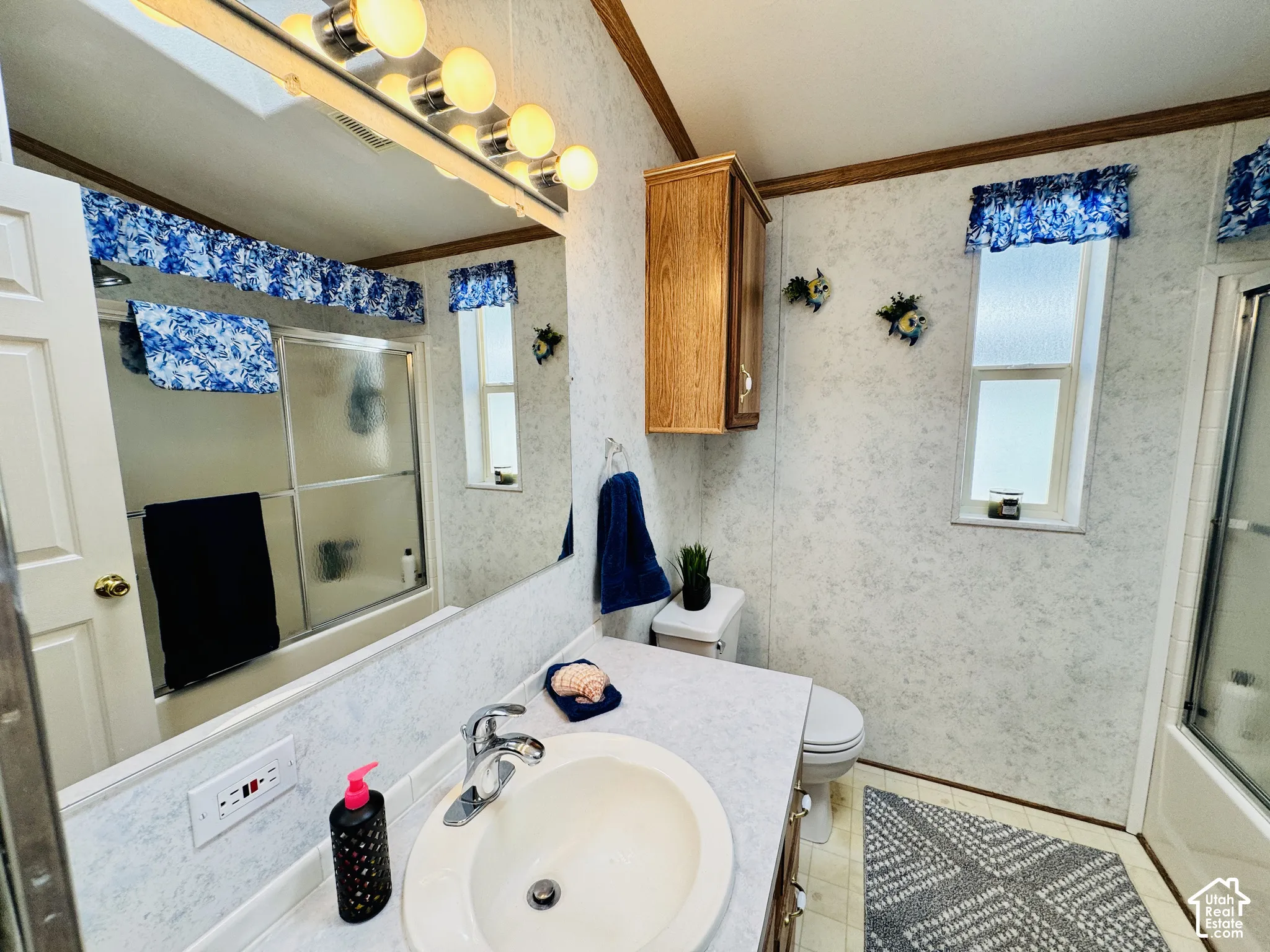 Bathroom featuring a built-in vanity with an integrated sink, wall-mounted light fixture, shower with sliding glass doors, and a window
