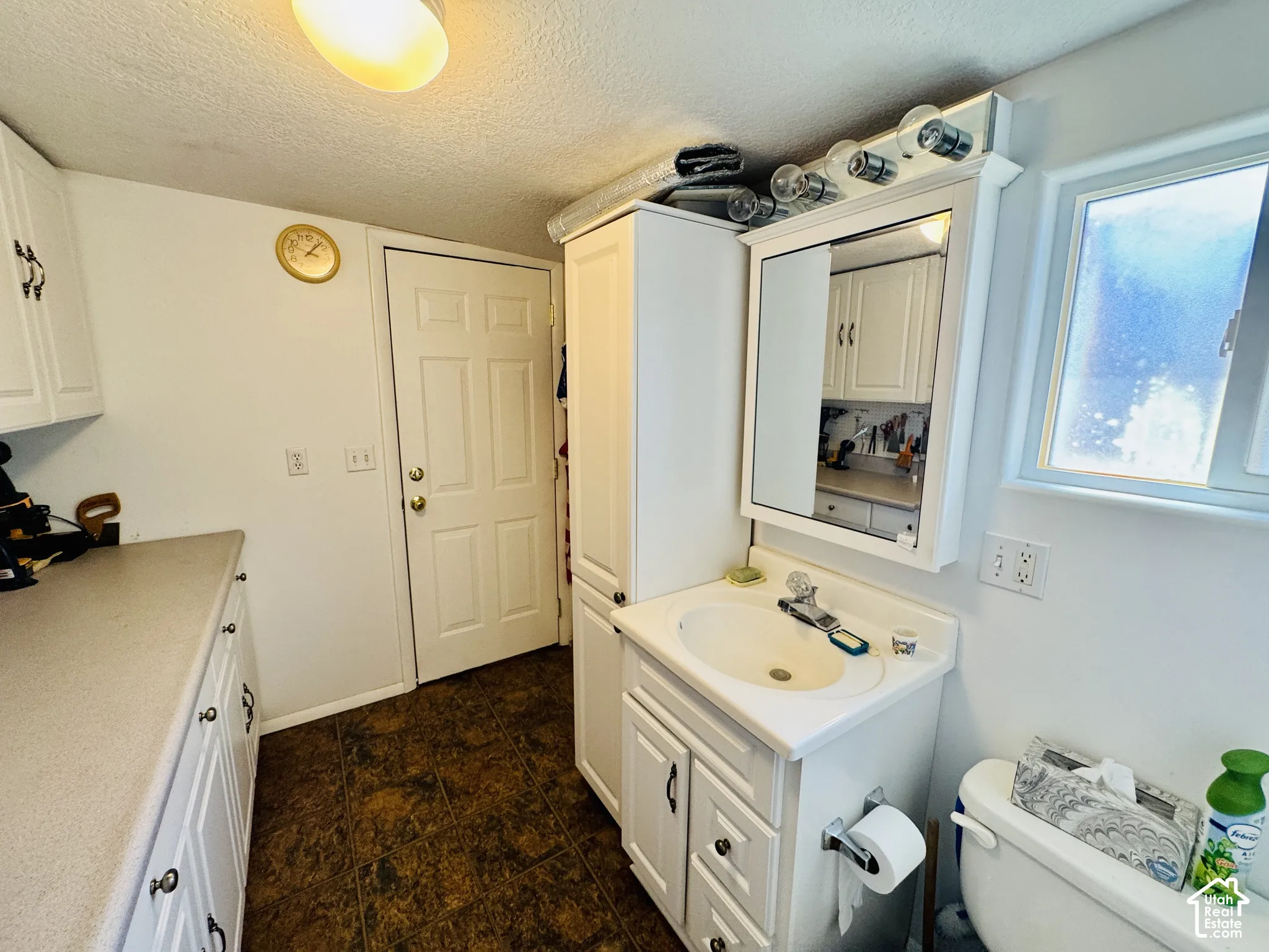 White cabinetry with dark hardware, a single-sink vanity, a wall-mounted mirror, and a built-in toilet