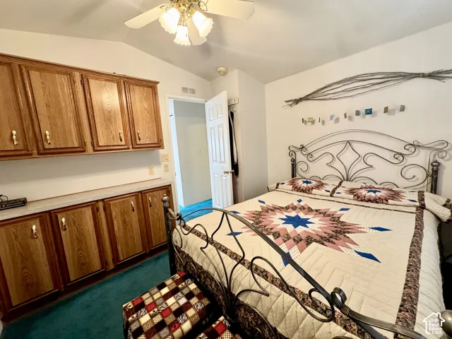 Vaulted ceiling with a ceiling fan, wall-mounted cabinetry, and a built-in countertop