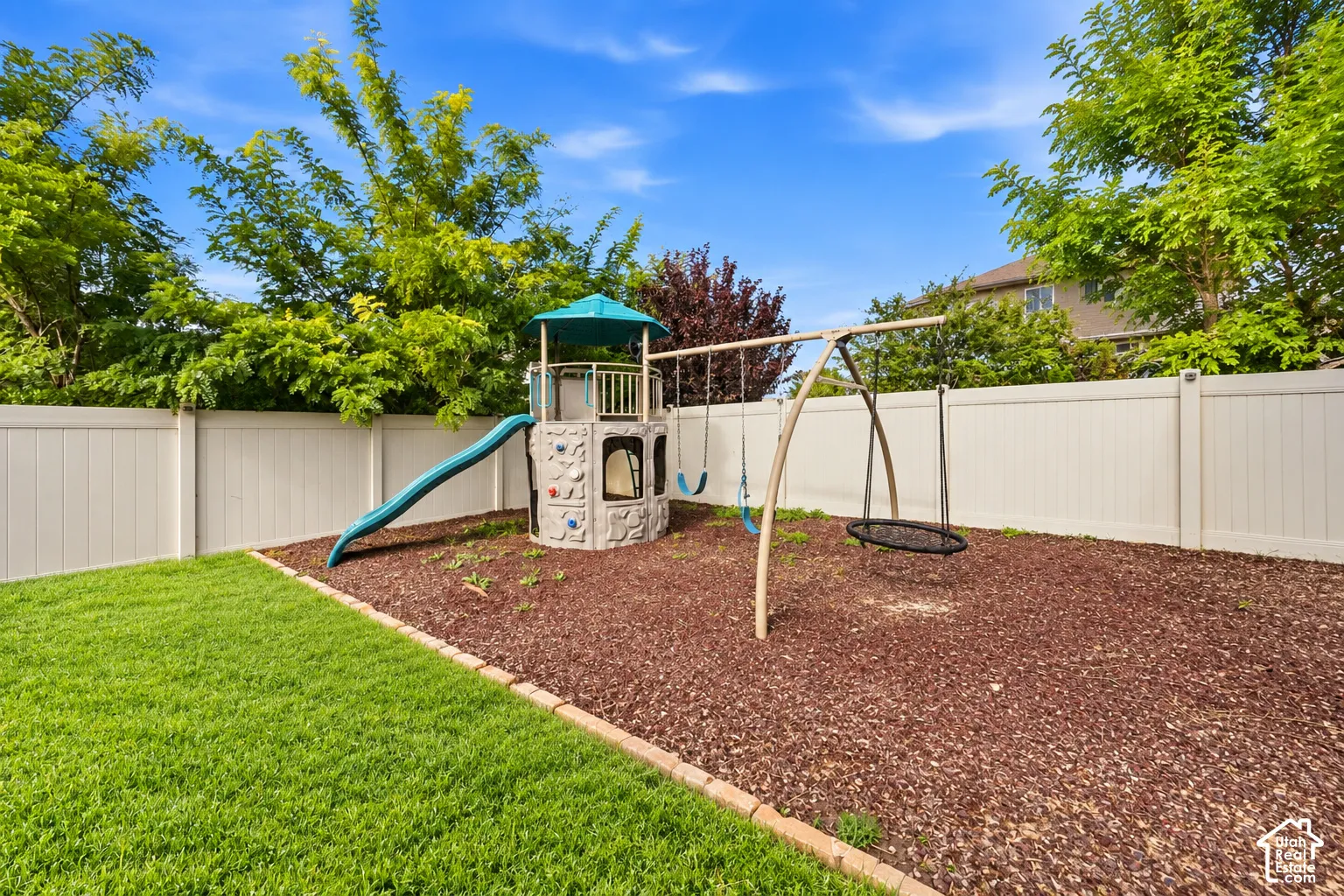 Expansive backyard featuring a manicured lawn, white privacy fence, and mature trees