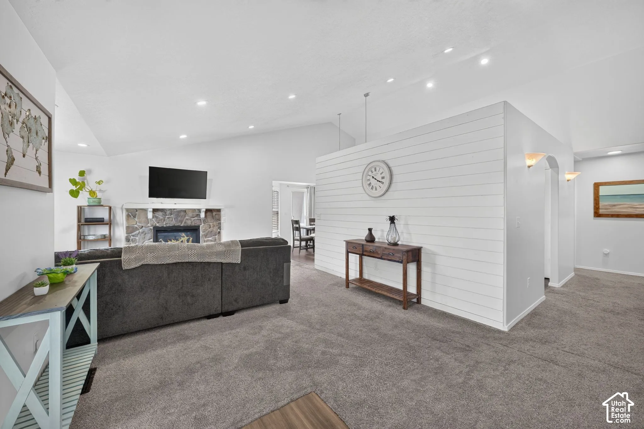 Vaulted ceiling, recessed lighting, stone-clad fireplace with mantel, shiplap accent wall, and arched entryway