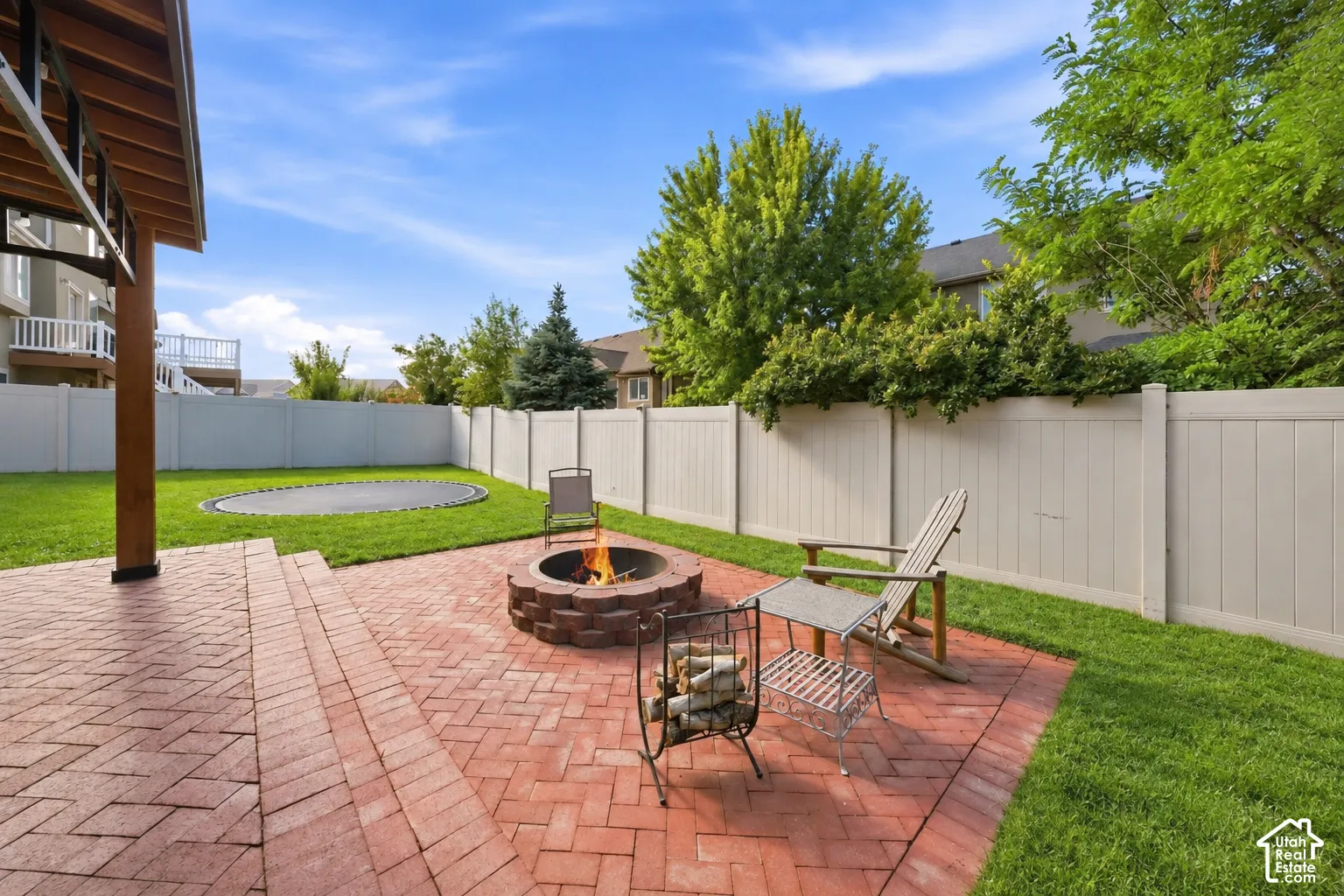 Red brick paver patio with a built-in fire pit, expansive lawn, and a light-colored privacy fence