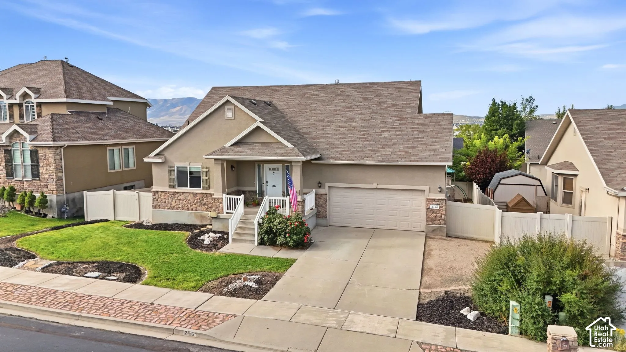 Stucco exterior with stone accents, covered front porch, attached garage, and a manicured lawn with mature landscaping
