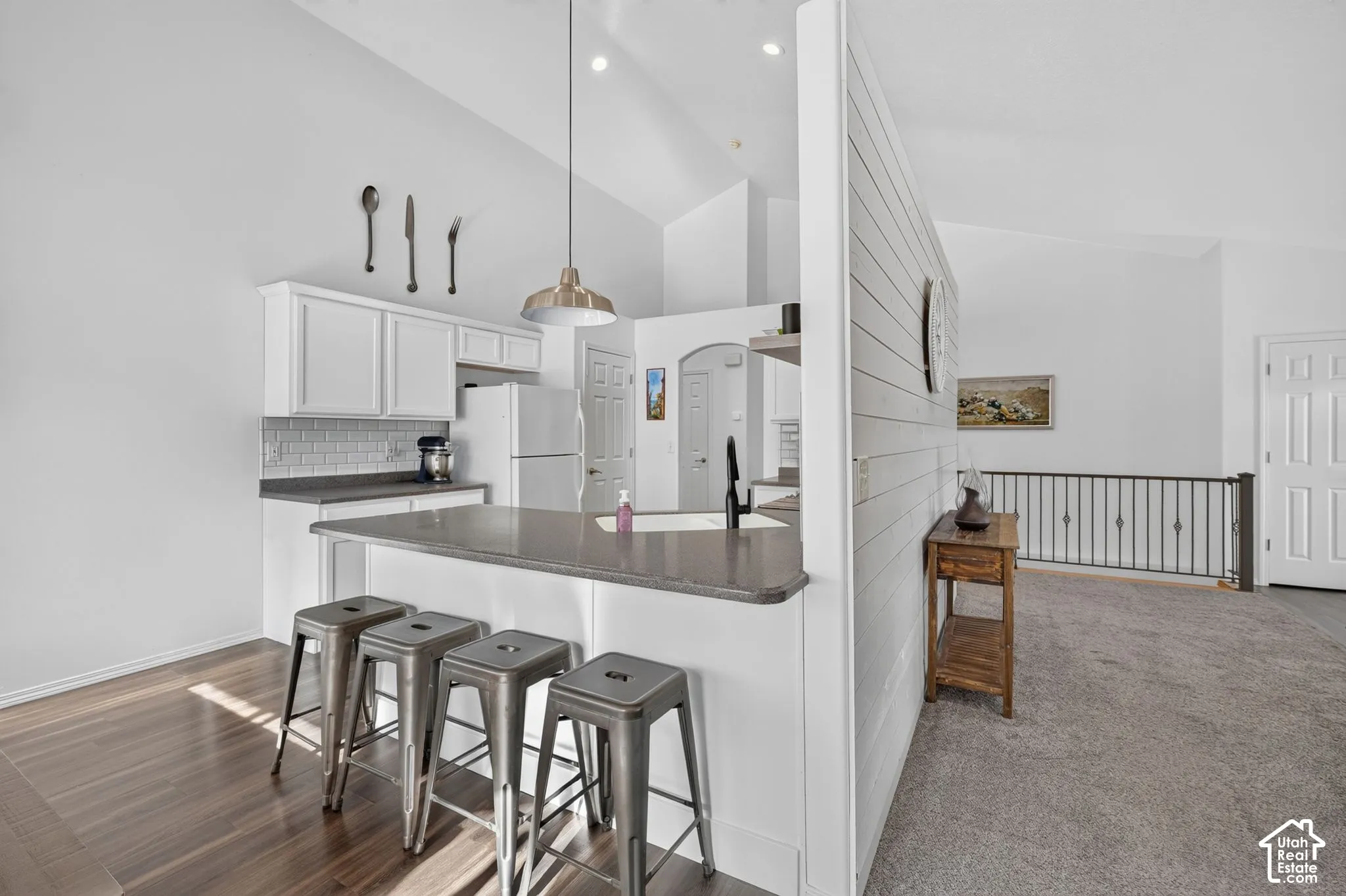 Kitchen island with seating, white shaker-style cabinetry, subway tile backsplash, and wood-finish flooring